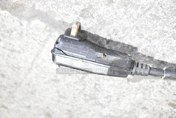 Close-up of Ryobi 1700 PSI electric pressure washer's power cord plug. Plug shows wear, with visible cracks on casing.