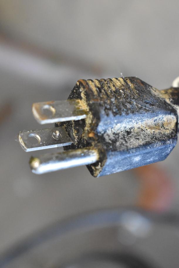 A dirty, close-up view of a power plug with metal prongs and a blackened surface, possibly indicating wear or damage.