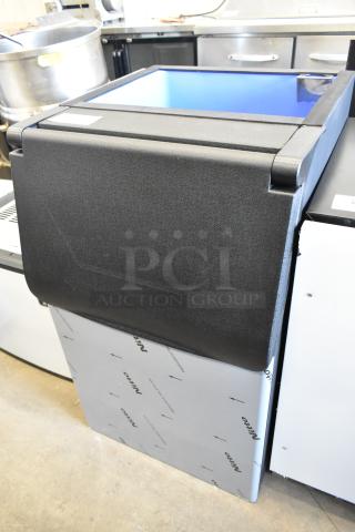 Brand new scratch and dent commercial metal ice bin with protective covering. Black top hatch, silver sides with visible brand logos.