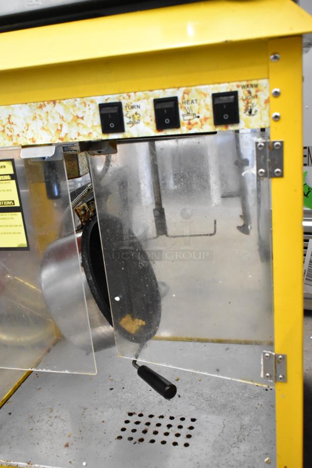 Metal commercial countertop popcorn machine, 115 volts, 1 phase. Features yellow trims, switches labeled for operation, and hinged door.