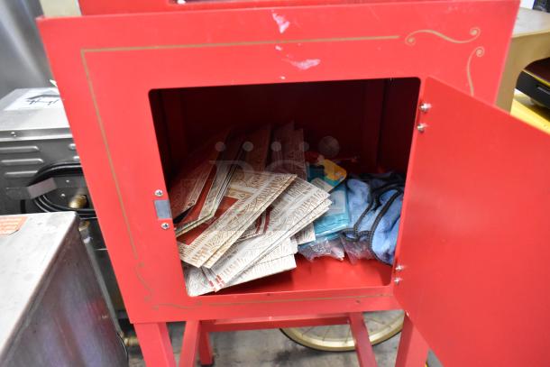 Nostalgia CCP510 popcorn machine, red metal with gold trim, open cart door showing accessories inside. 115 volts, 1 phase.