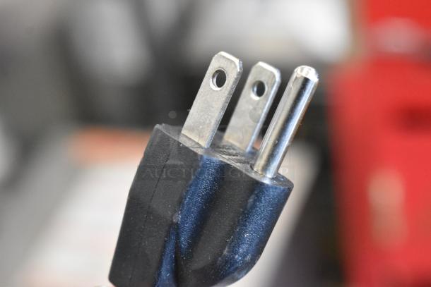 Close-up image of a three-prong electrical plug, showing metal prongs and a black plastic casing.