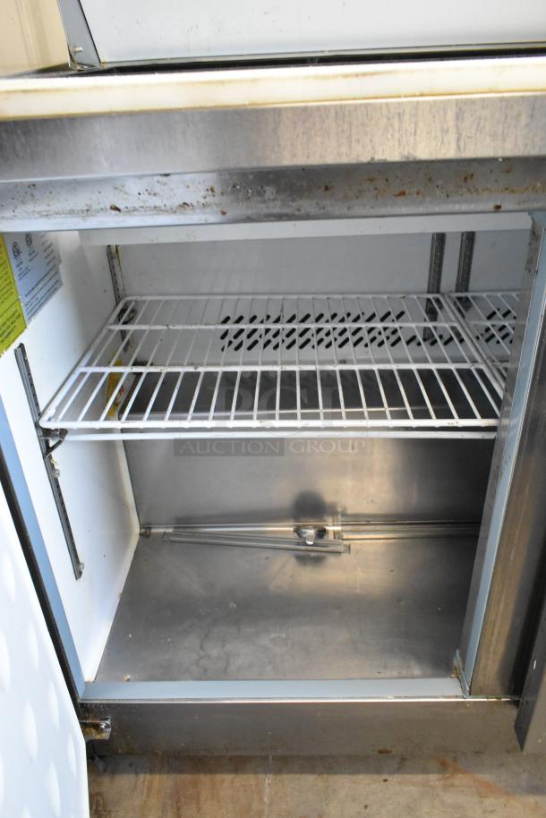 Ikon KSP48 stainless steel sandwich prep table, visible interior shelves, used condition, on commercial casters.