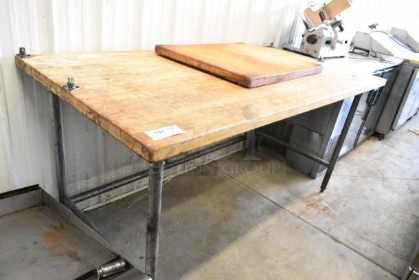 Butcher block wooden table with metal legs, worn surface, includes rectangular board, ID tag visible, sturdy construction.