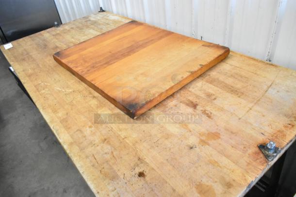 Butcher block wooden table with metal legs, showing wear and surface marks. Ideal for kitchens or workshops.