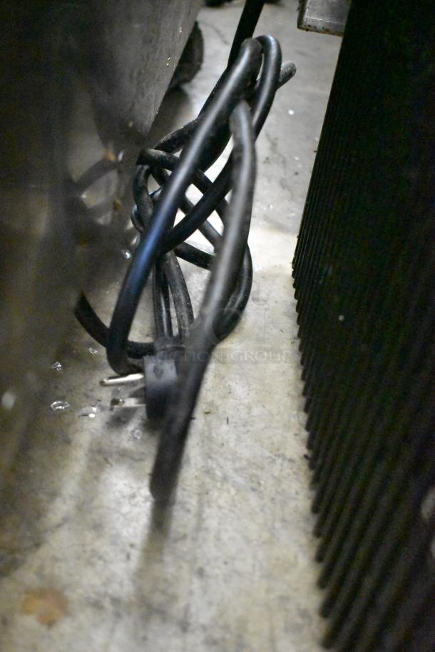 Power cord of True T-23F-HC commercial freezer, coiled and unplugged on concrete floor. 115 volts, 1 phase.