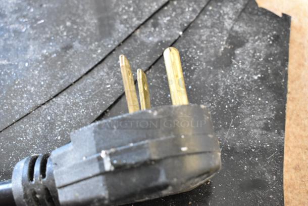 Close-up of a power plug for an induction range, showing three prongs against a dark surface.