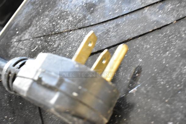 Close-up of a power plug showing standard prongs against a textured black surface. Part of auction lot with induction ranges.