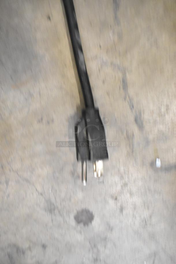 Power cord for Hoshizaki F-330BAJ ice machine, black, two-prong plug, on concrete surface.