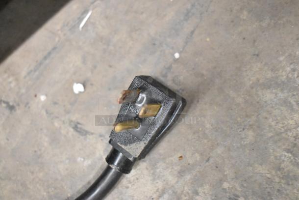 Black power cord for True GEM-49 cooler, standard three-prong plug on industrial concrete floor.
