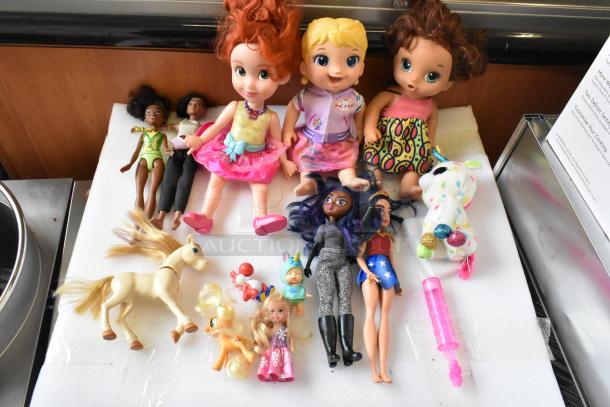 Lot of various items including dolls, Barbies, and stuffed animals. Features diverse doll types and colorful clothing.