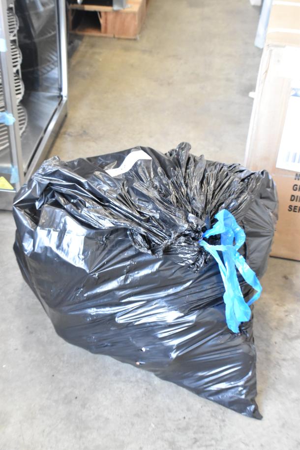 A large black garbage bag tied with blue twine, containing various items like dolls, Barbies, and stuffed animals.