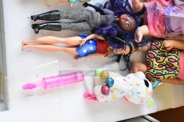 Lot of dolls, Barbies, and stuffed animals, featuring a superhero doll, colorful outfits, and a plush unicorn. Good condition.