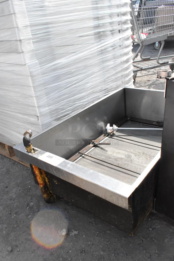 Metal commercial grease trap in used condition, featuring a mesh screen and piping. Label reads "205," indicating identification.