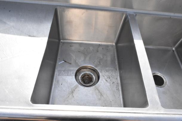 Stainless steel 3 bay sink with dual drain boards, visible wear, and drain strainers. Ideal for commercial use.