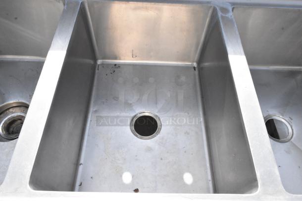 Stainless steel 3 bay sink with dual drain boards, visible signs of wear. Ideal for commercial kitchens.