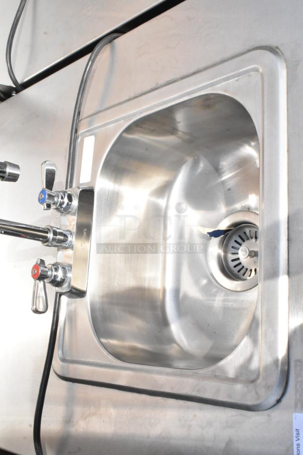 QualServ stainless steel commercial portable sink with dual taps, shown in good condition, includes commercial casters.