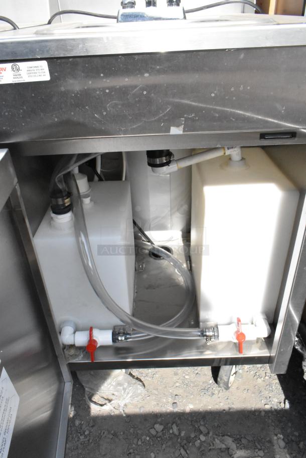 QualServ stainless steel portable sink with casters, showing under-sink plumbing, water tanks, and pipes, well-maintained.