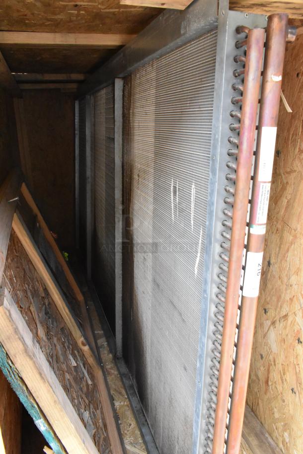 Brand new evaporator coil in crate, metal fins, copper pipes with labels, indicating model and serial number.