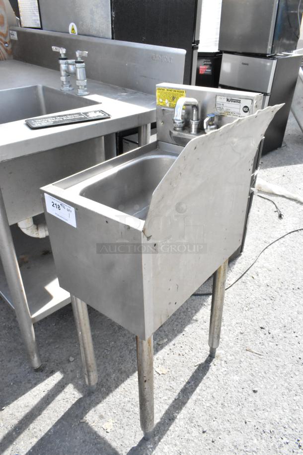 Stainless steel single bay sink with side splash guard, dual faucets, and sturdy legs. Good condition with visible labels.