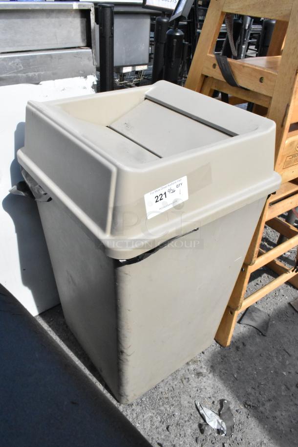 Tan poly trash can with swing lid, visible wear and scuff marks, auction tag labeled "221", approximate standard size.