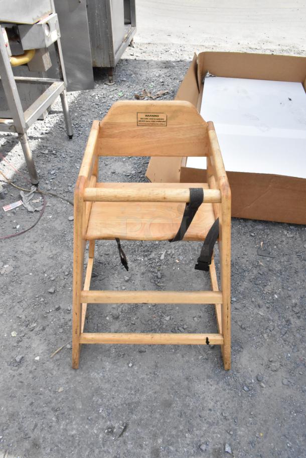 Wooden high chair with natural finish, visible safety label, and black straps. Solid condition, used outdoors. Set of three.