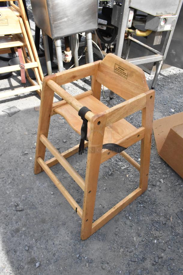 Wooden high chair with natural finish, harness strap, and warning label. Good condition, suitable for restaurant or home use.