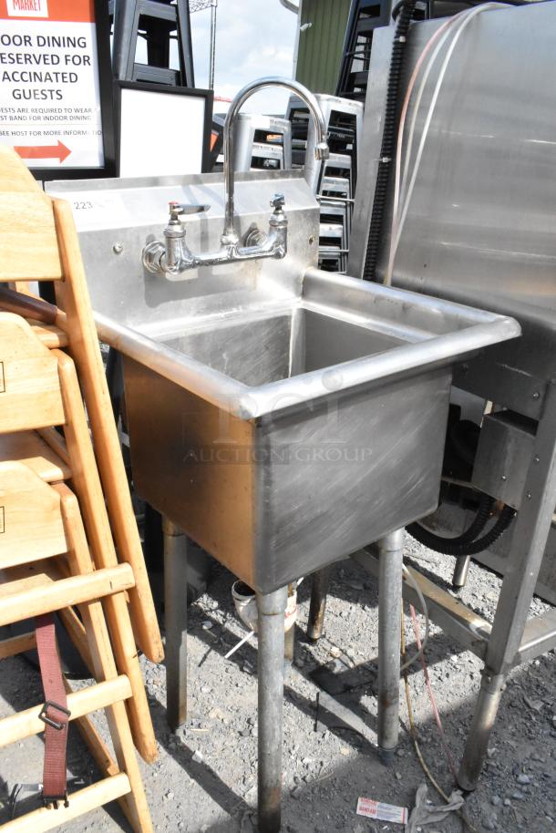Stainless steel single bay sink with dual faucet handles, mounted on sturdy legs, in good condition.