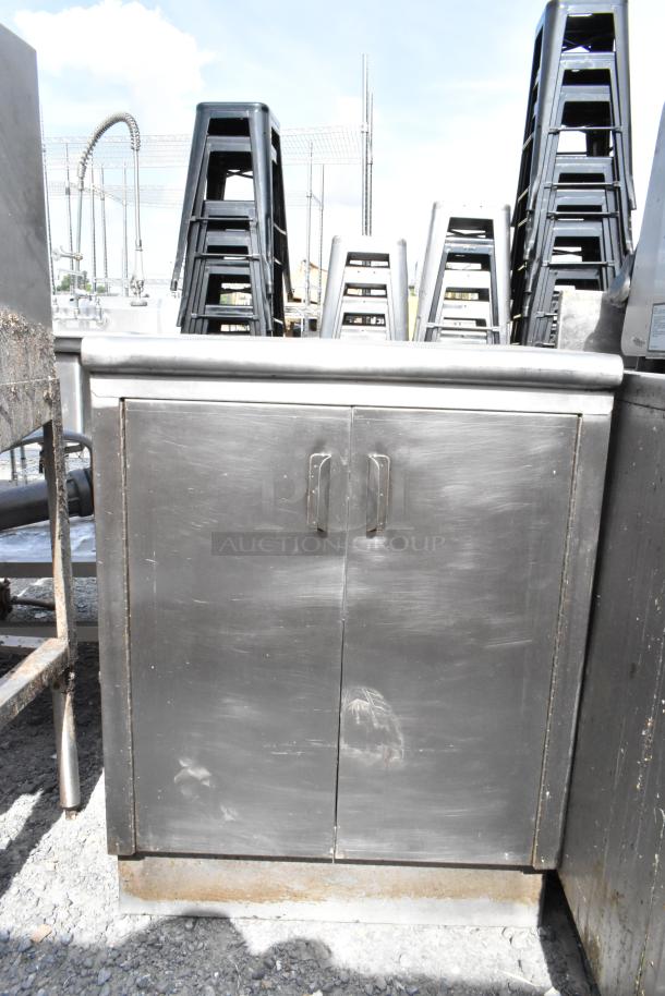 Stainless steel table with two doors and two under shelves. Features a brushed finish and sturdy handles. Visible wear consistent with outdoor use.