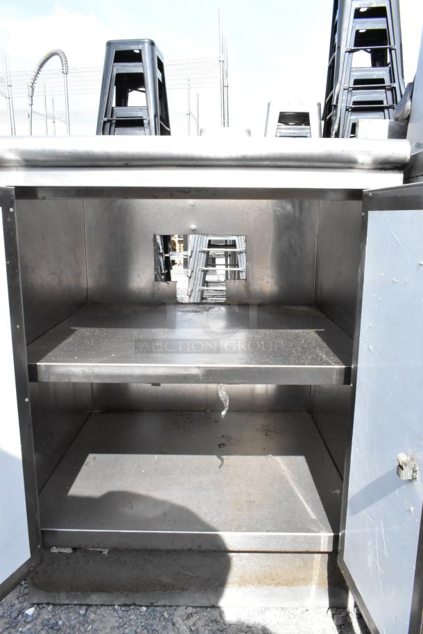 Stainless steel table with 2 doors and 2 under shelves, showing storage space. Note some wear and minor scratches visible.
