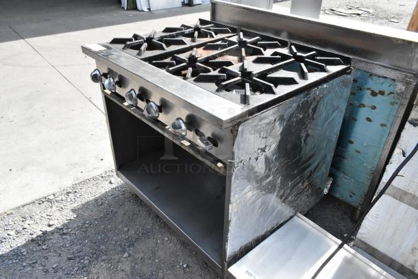 Stainless steel commercial gas-powered 6 burner range with under shelf. Features control knobs, sturdy construction. Signs of use.