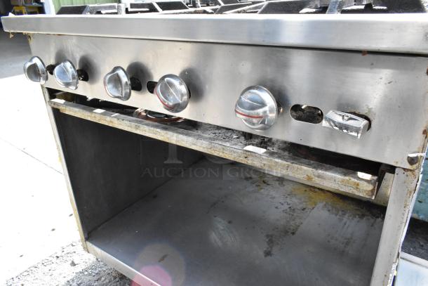 Stainless steel commercial 6-burner gas range with under shelf. Features control knobs and open under storage. Used condition.