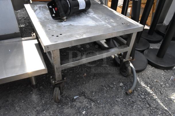 Stainless steel equipment stand on casters and a shelf, used condition, with visible wear. Includes additional hardware.