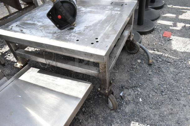 Stainless steel equipment stand with attached shelf, on casters, visible wear, suitable for industrial use.