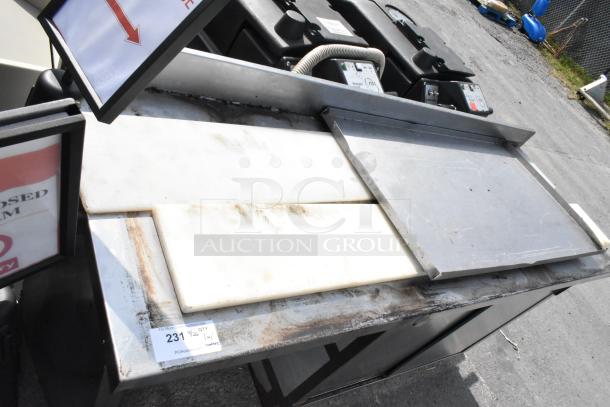 Stainless steel table with doors and under shelf; scratched surface; auction tag "231" shown; outdoor setting.