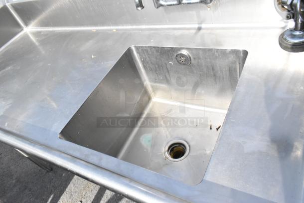 Stainless steel single bay sink with faucet and spray nozzle attachment, visible signs of use, suitable for commercial kitchens.
