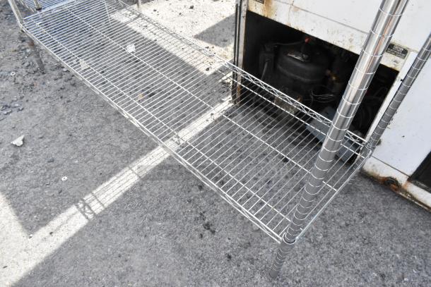 Chrome finish 3-tier wire shelving unit in used condition, outdoors on pavement. Buyer must dismantle. Consider freight charges.