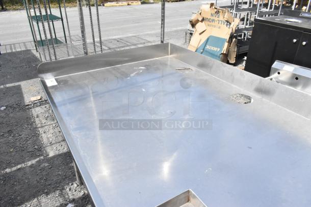 Stainless steel soda station with under shelves, features dual cutouts, minor surface scratches, outdoor setting.
