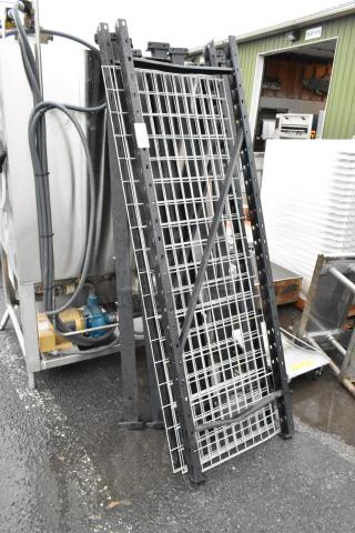 Lot of metal shelving units with wire grids and black frames, upright and stacked outdoors, showing light wear.