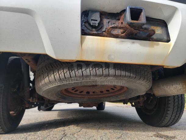 Underside view of 2012 Chevy Tahoe 4x4 showing spare tire, hitch receiver, and some rusted components.