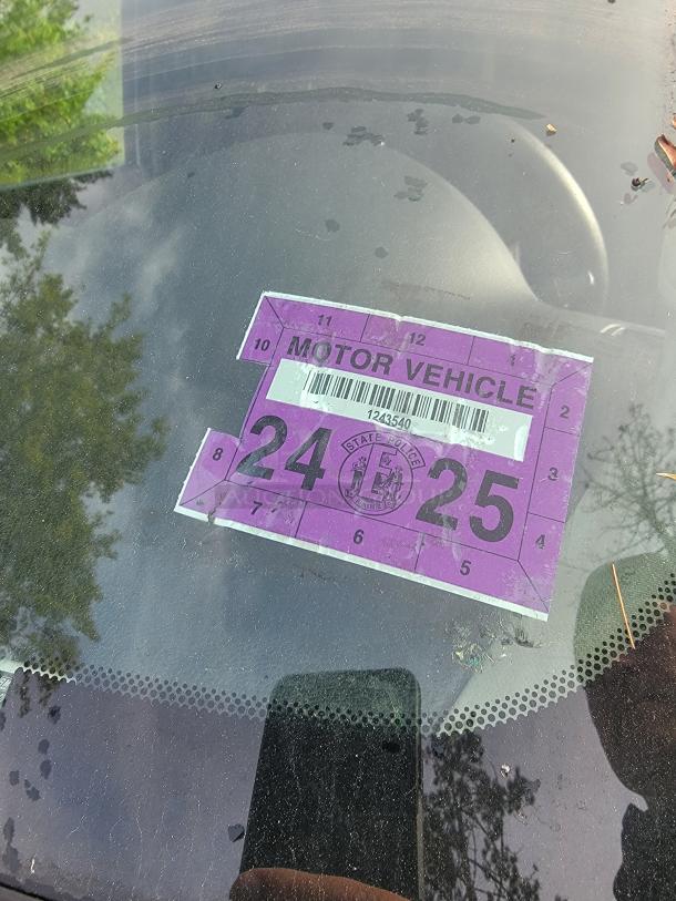 Close-up of a purple 2024-2025 motor vehicle inspection sticker on a 2012 Chevy Tahoe windshield.