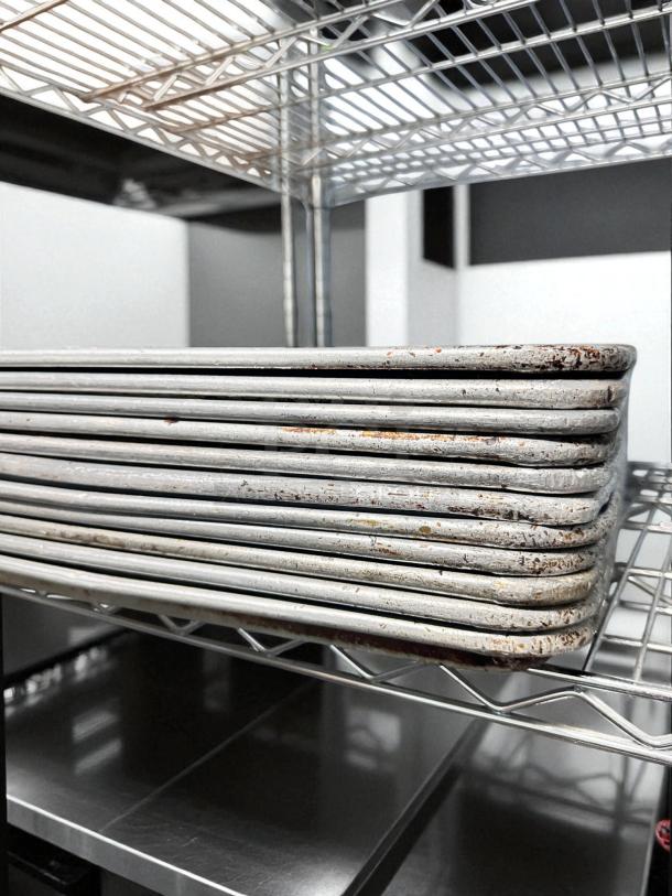 Set of commercial full-size sheet pans in excellent condition, stacked on a metal rack, ready for use, unbranded.