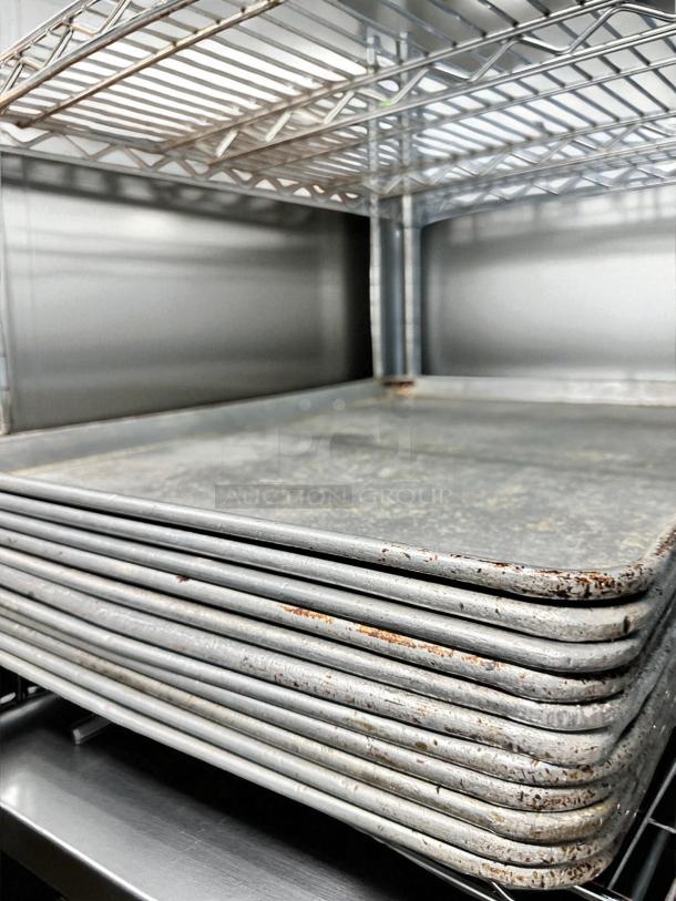 Stack of unbranded commercial full-size sheet pans in excellent condition on a metal rack, ready for use.
