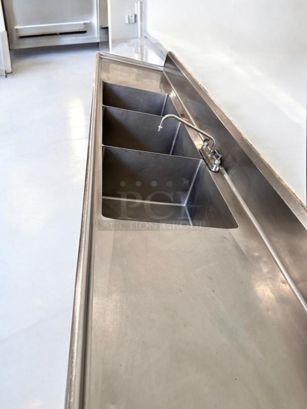 Three-compartment stainless steel sink with dual drainboards, fully operational, excellent condition, commercial grade.