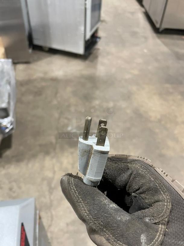 A hand wearing a glove holding a three-prong electrical plug, associated with Univex SRM20 mixer, shown in an industrial setting.