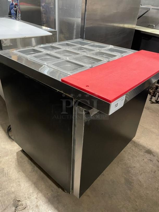 Continental SW32-12M black refrigerated prep table with stainless top, red cutting board, clear pans, poly rack, on casters.