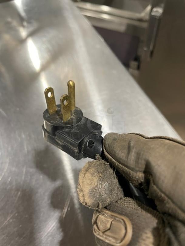 Gloved hand holding a power plug of the True TWT60 stainless steel refrigerator. Plug detail shown for condition.