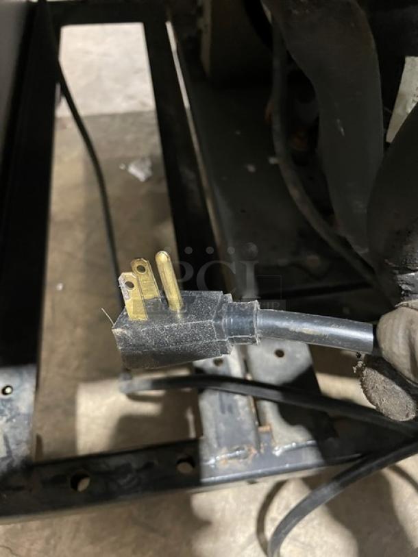 Close-up of a power plug for a True T-23 commercial refrigerator, showing three prongs. Electrical cord extends from the plug.