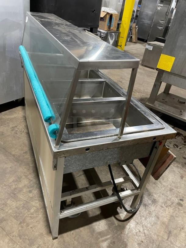 Atlas Metal stainless steel 4-well steam table with sneeze guard, tray slide, 208V, 1 phase, on casters.