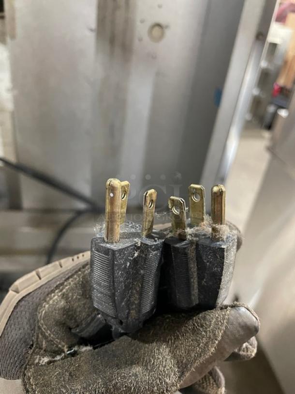This image shows a close-up of electrical plugs being held in a gloved hand, related to the Blodgett convection oven auction item.